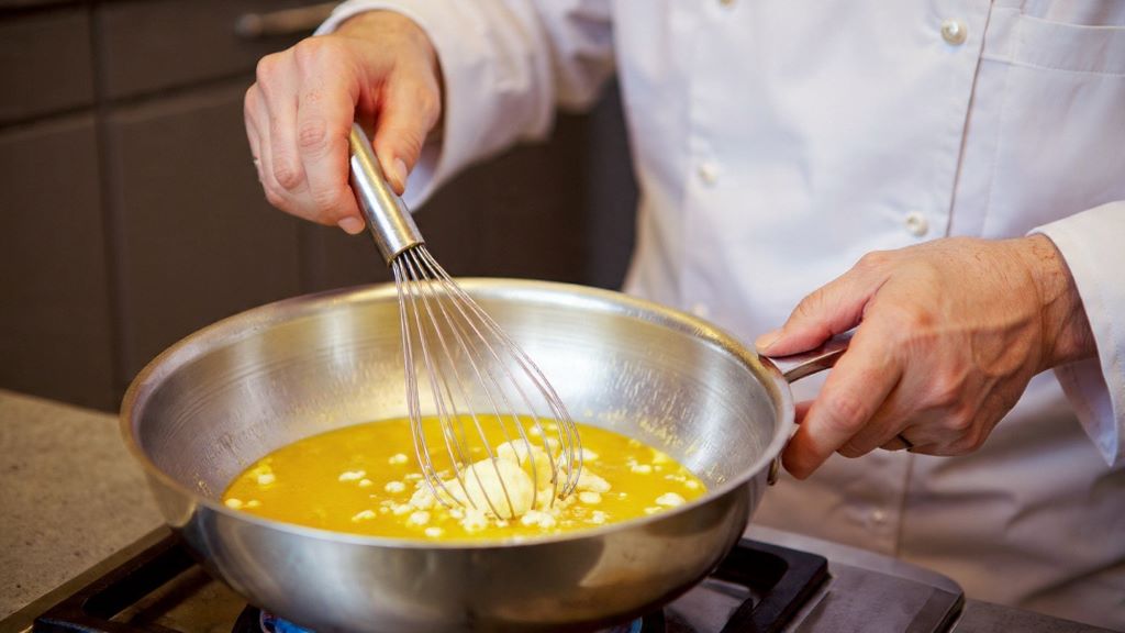 Chef whisking butter into lemon sauce in stainless steel pan for balanced flavor